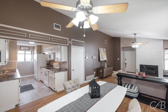 dining room with lofted ceiling, ceiling fan, sink, light hardwood / wood-style flooring, and a stone fireplace