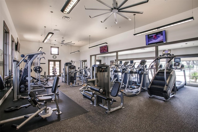 gym featuring ceiling fan, plenty of natural light, and a towering ceiling