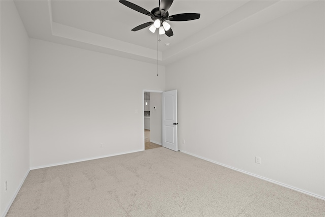 empty room with ceiling fan, a tray ceiling, and light carpet