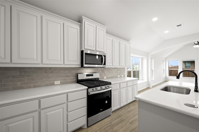 kitchen with sink, appliances with stainless steel finishes, backsplash, white cabinets, and vaulted ceiling