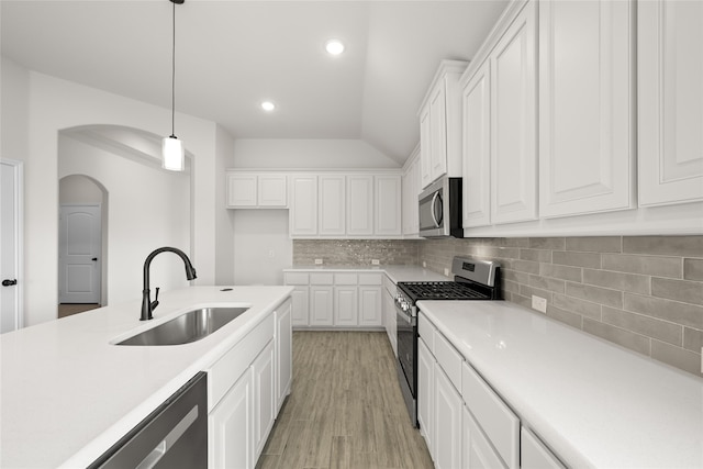 kitchen with sink, stainless steel appliances, vaulted ceiling, decorative light fixtures, and white cabinets