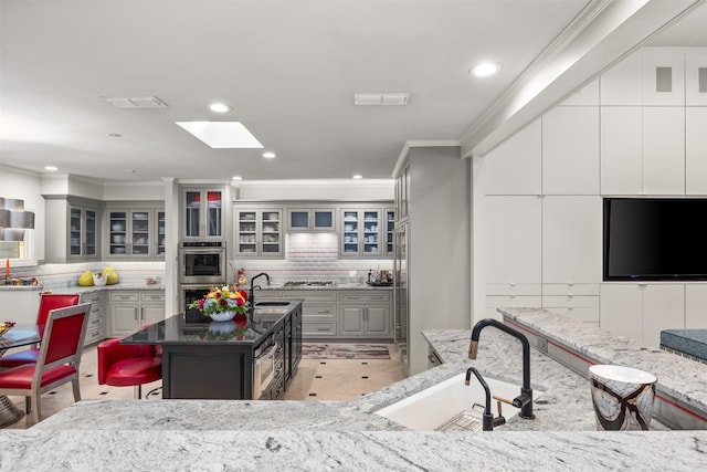 kitchen featuring tasteful backsplash, a kitchen island with sink, a kitchen breakfast bar, and gray cabinets