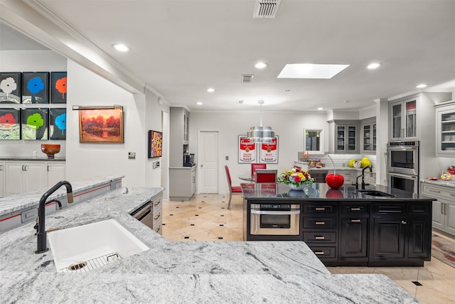 kitchen featuring double oven, light stone countertops, and sink