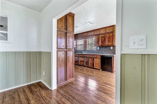 kitchen with decorative backsplash, black dishwasher, dark hardwood / wood-style flooring, a textured ceiling, and ornamental molding