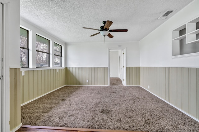 spare room featuring wood walls, a textured ceiling, carpet flooring, and ceiling fan