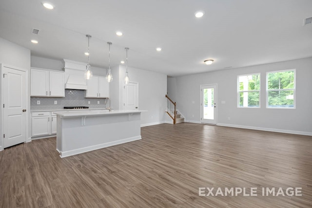 kitchen with tasteful backsplash, a kitchen island with sink, pendant lighting, hardwood / wood-style floors, and white cabinetry