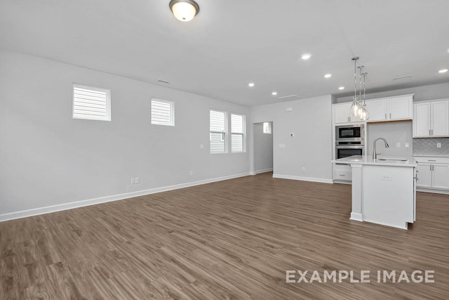 kitchen featuring stainless steel appliances, dark wood-type flooring, decorative light fixtures, white cabinets, and an island with sink