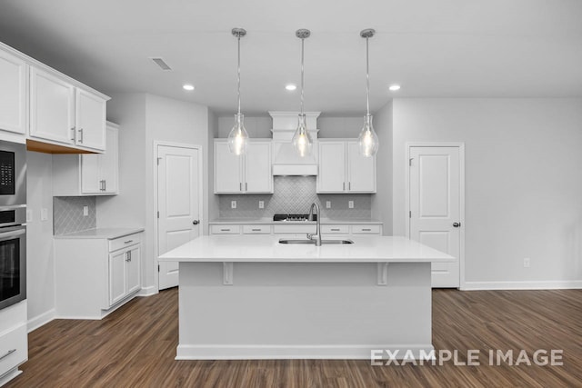 kitchen with hanging light fixtures, dark hardwood / wood-style floors, white cabinetry, and a kitchen island with sink