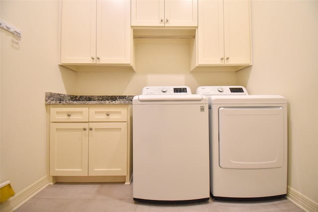 clothes washing area featuring cabinets, light tile patterned floors, and washer and clothes dryer