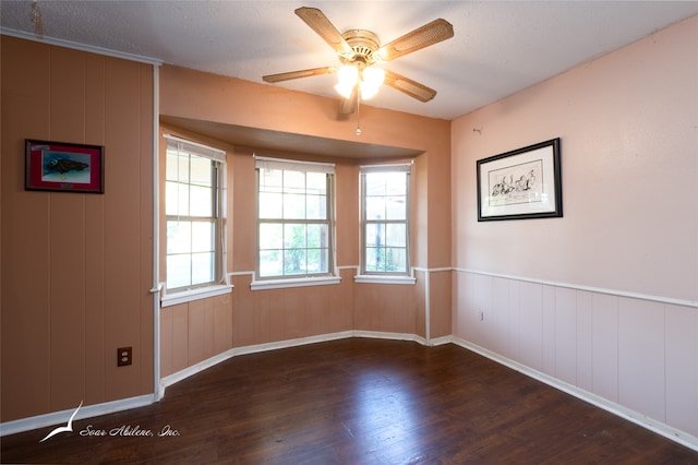 spare room featuring wood walls, a textured ceiling, dark wood-type flooring, and ceiling fan