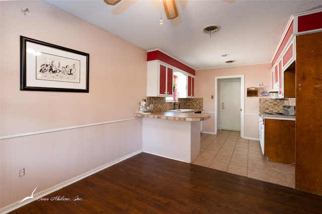 kitchen with kitchen peninsula, backsplash, sink, hardwood / wood-style floors, and electric stove