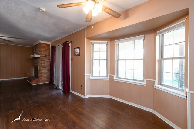 unfurnished living room featuring wooden walls, crown molding, dark hardwood / wood-style floors, and ceiling fan