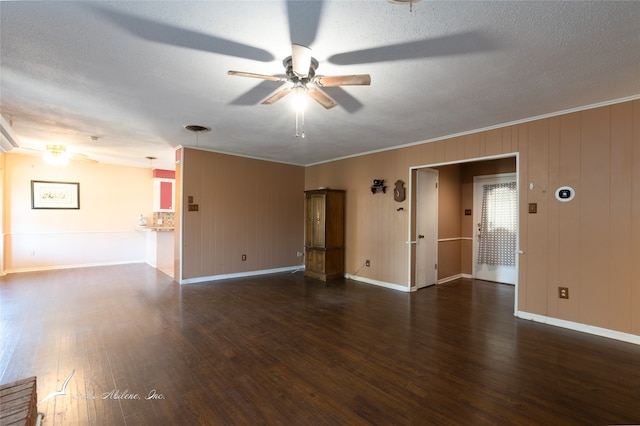 empty room with wood walls, a textured ceiling, ceiling fan, ornamental molding, and dark hardwood / wood-style floors