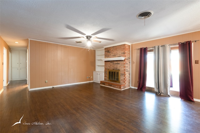 unfurnished living room with a textured ceiling, a brick fireplace, ceiling fan, dark wood-type flooring, and ornamental molding