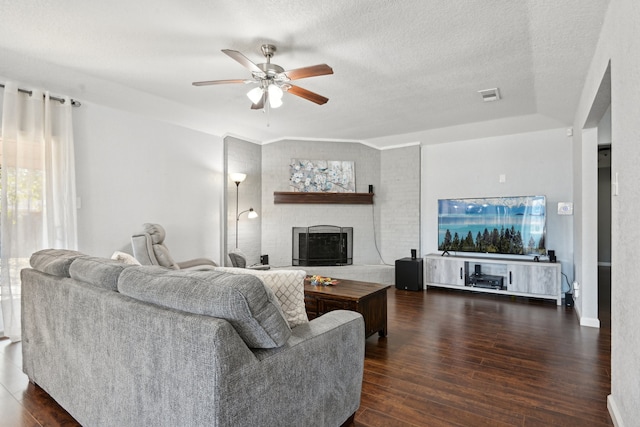 living room with dark wood-type flooring, a fireplace, a textured ceiling, and ceiling fan