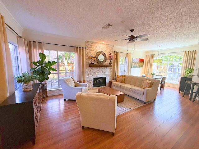 living room with hardwood / wood-style floors, ceiling fan, a textured ceiling, ornamental molding, and a fireplace