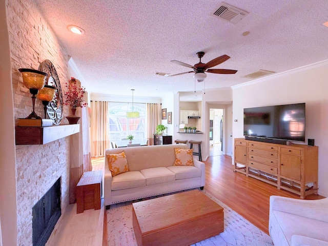 living room with ceiling fan, a textured ceiling, light hardwood / wood-style flooring, a fireplace, and crown molding