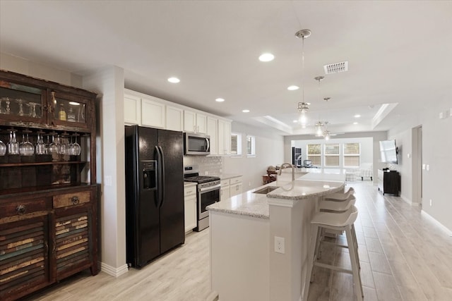 kitchen with sink, appliances with stainless steel finishes, an island with sink, a raised ceiling, and white cabinets