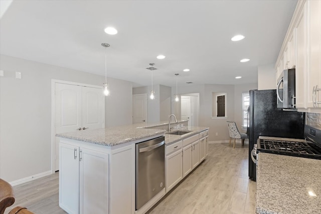 kitchen featuring white cabinets, stainless steel appliances, pendant lighting, and an island with sink