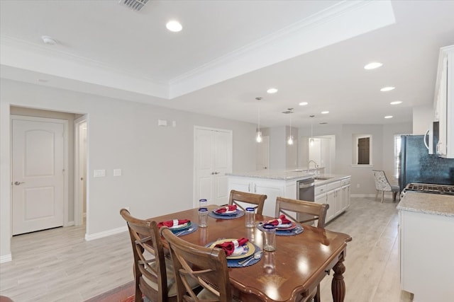 dining space featuring light hardwood / wood-style floors, a tray ceiling, sink, and ornamental molding