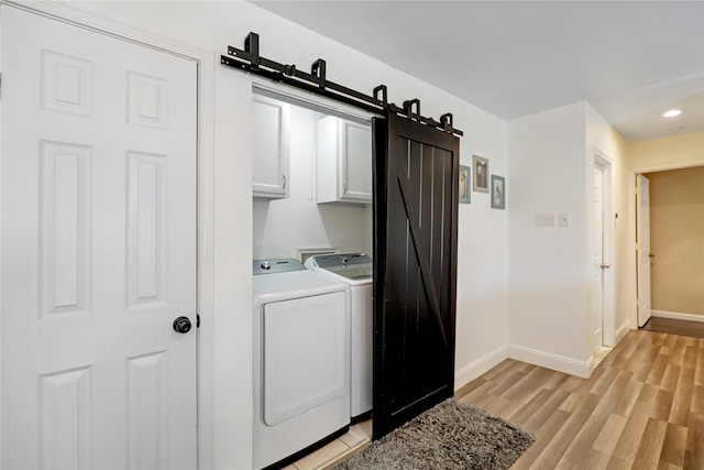 laundry area featuring cabinets, a barn door, separate washer and dryer, and light hardwood / wood-style flooring