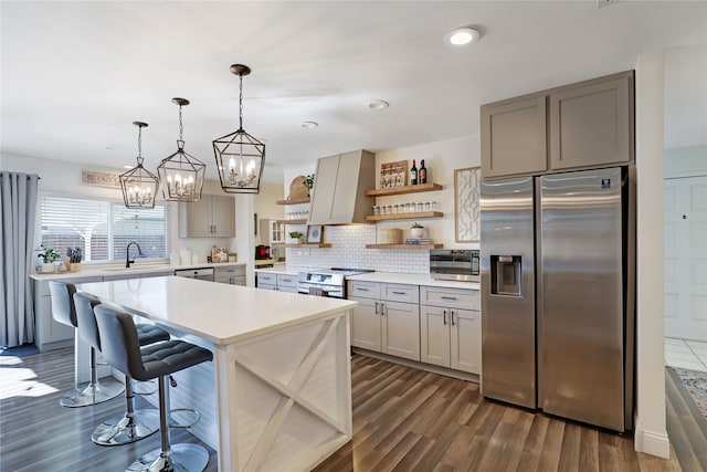 kitchen with sink, appliances with stainless steel finishes, a kitchen breakfast bar, hanging light fixtures, and dark hardwood / wood-style flooring