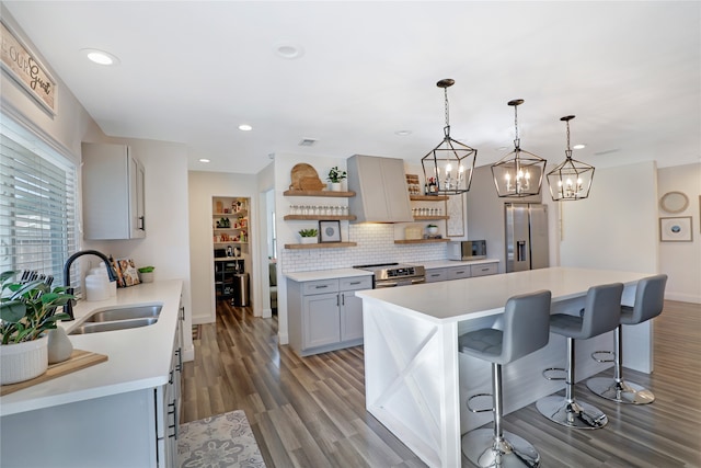 kitchen featuring sink, appliances with stainless steel finishes, decorative light fixtures, wood-type flooring, and a center island