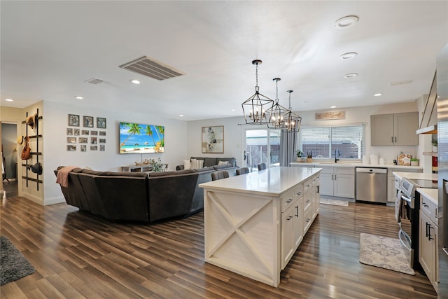 kitchen with a kitchen island, appliances with stainless steel finishes, dark hardwood / wood-style floors, hanging light fixtures, and an inviting chandelier