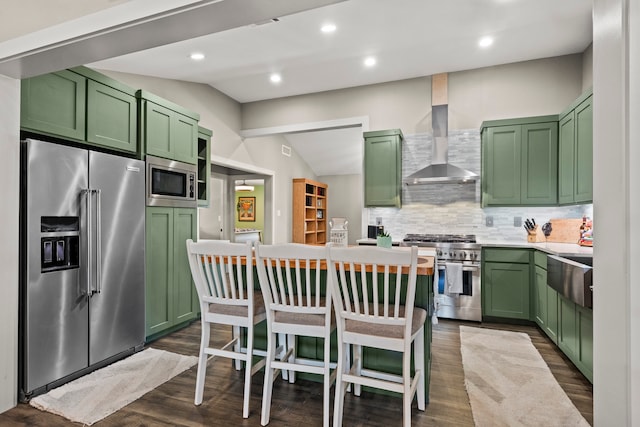 kitchen with wall chimney exhaust hood, high quality appliances, green cabinets, vaulted ceiling, and dark hardwood / wood-style flooring