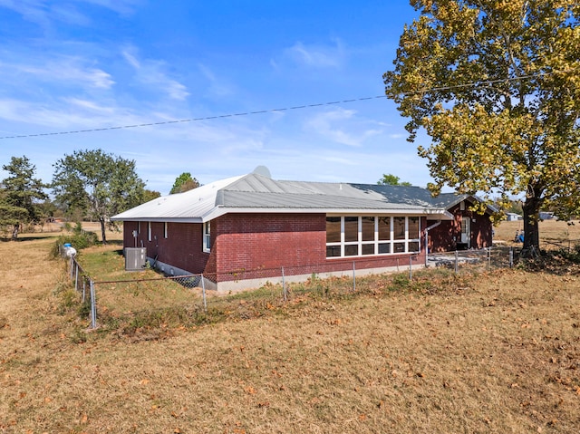 view of home's exterior featuring central air condition unit, a sunroom, and a lawn