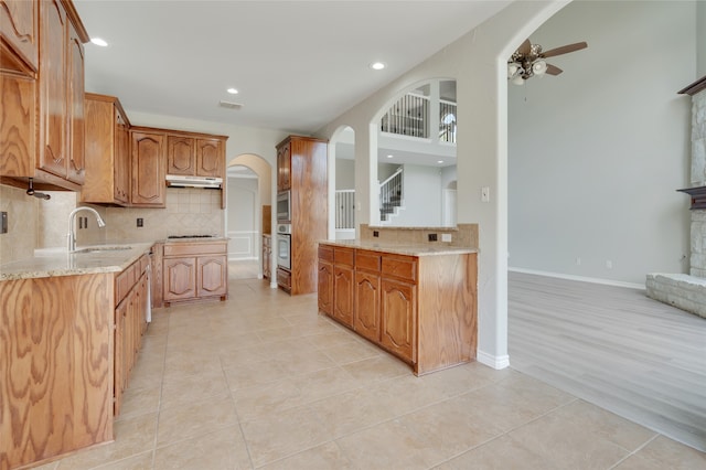 kitchen with tasteful backsplash, sink, stainless steel appliances, light stone counters, and light tile patterned floors