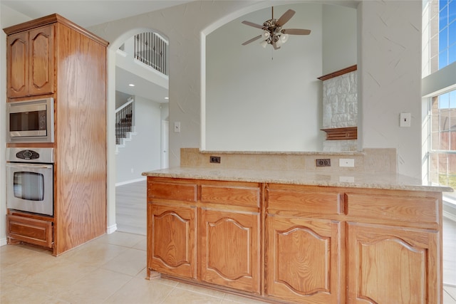 kitchen with kitchen peninsula, stainless steel appliances, light tile patterned flooring, light stone counters, and a towering ceiling