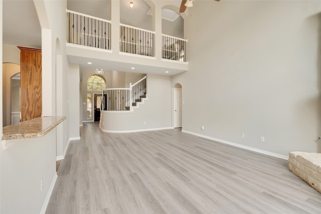 unfurnished living room with a towering ceiling, light hardwood / wood-style flooring, and ceiling fan