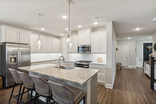 kitchen with hanging light fixtures, a center island with sink, sink, white cabinetry, and appliances with stainless steel finishes