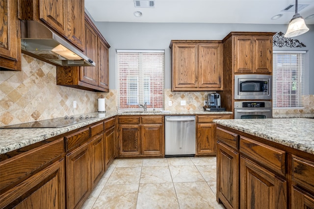 kitchen featuring decorative backsplash, light stone counters, appliances with stainless steel finishes, sink, and decorative light fixtures