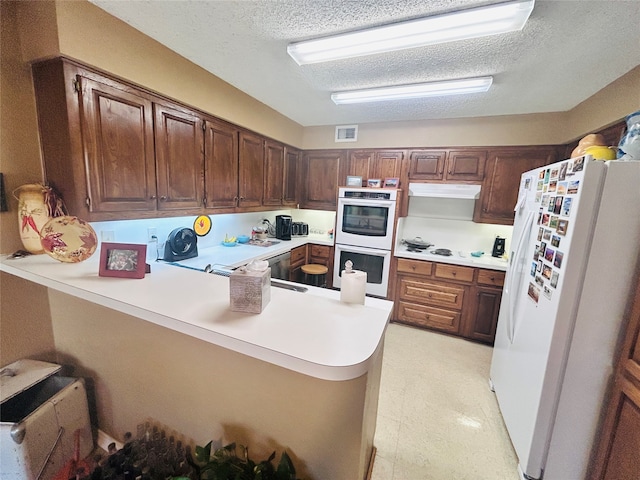 kitchen featuring kitchen peninsula, a textured ceiling, and white appliances