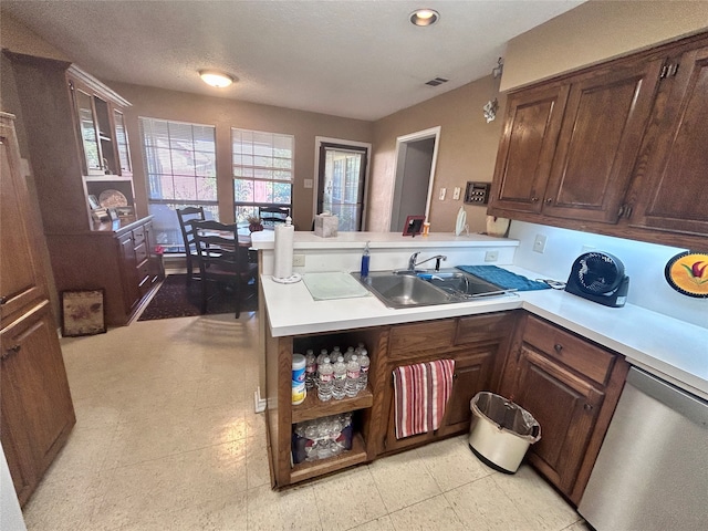 kitchen featuring kitchen peninsula, dark brown cabinets, a textured ceiling, dishwasher, and sink