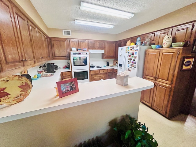 kitchen featuring white appliances, a textured ceiling, and kitchen peninsula