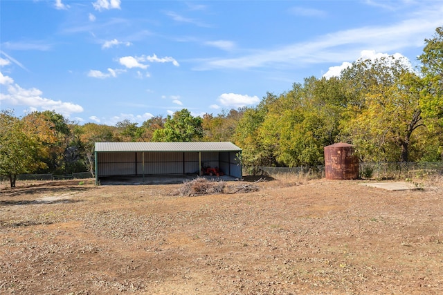 view of pole building with driveway, a wooded view, fence, and a detached carport