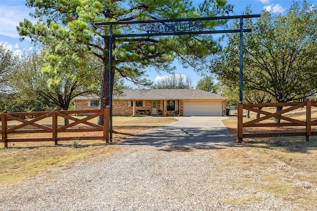 ranch-style home featuring an attached garage, gravel driveway, a gate, fence, and brick siding