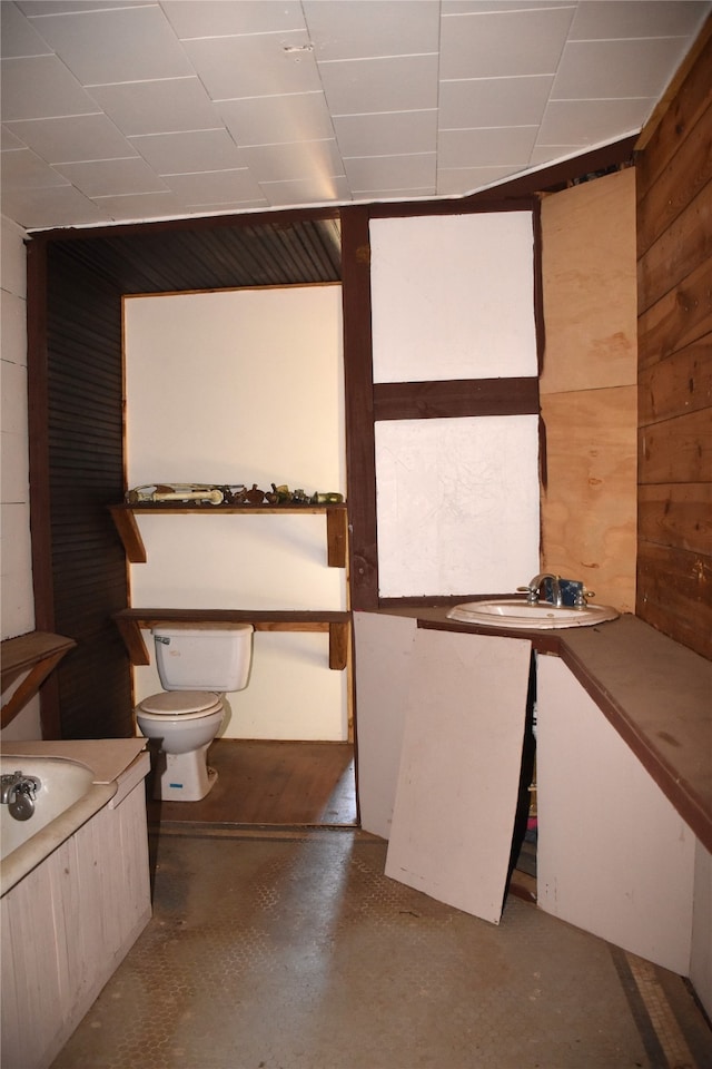 bathroom with a bathtub, concrete flooring, toilet, and wood walls