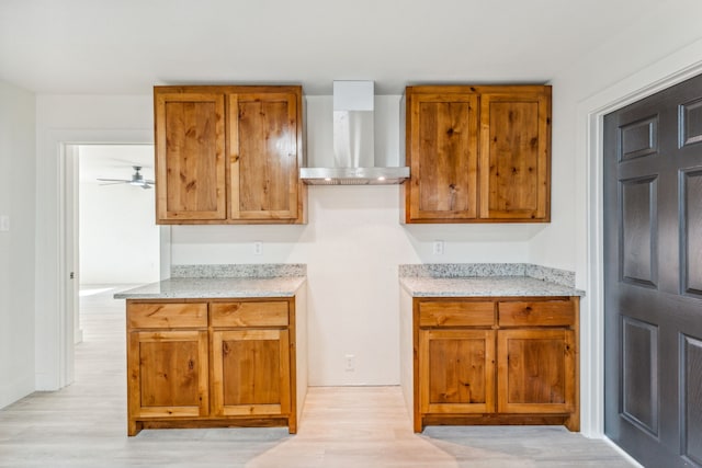 kitchen with ceiling fan, light hardwood / wood-style flooring, light stone counters, and wall chimney range hood