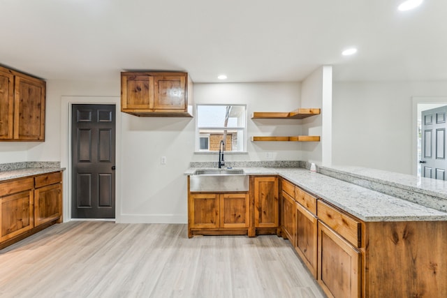 kitchen with kitchen peninsula, light hardwood / wood-style floors, light stone counters, and sink