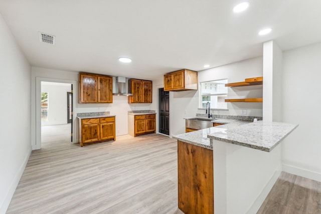 kitchen featuring wall chimney exhaust hood, light stone counters, plenty of natural light, and light hardwood / wood-style flooring