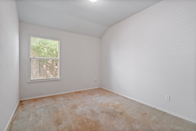 carpeted spare room featuring vaulted ceiling and baseboards