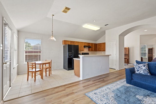 kitchen with black refrigerator with ice dispenser, a kitchen island, vaulted ceiling, light hardwood / wood-style floors, and decorative light fixtures