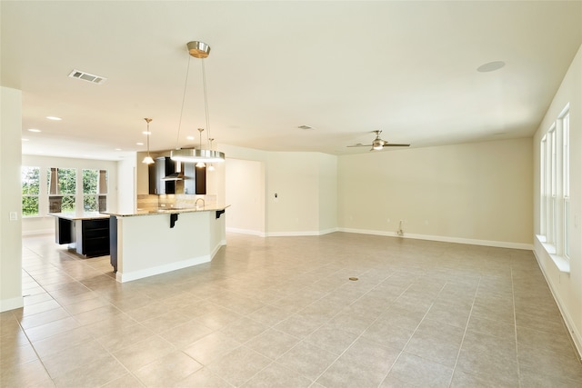 interior space with pendant lighting, backsplash, a spacious island, wall chimney range hood, and a kitchen bar