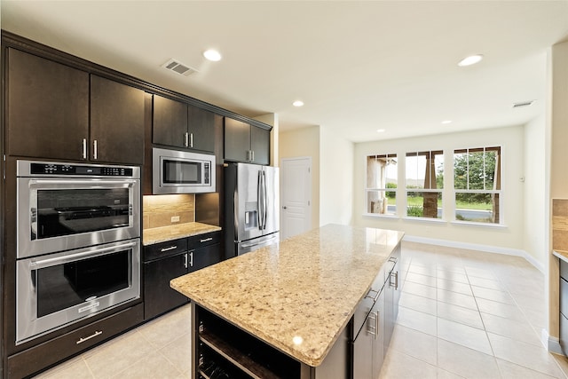 kitchen featuring a center island, light tile patterned floors, light stone countertops, appliances with stainless steel finishes, and dark brown cabinets