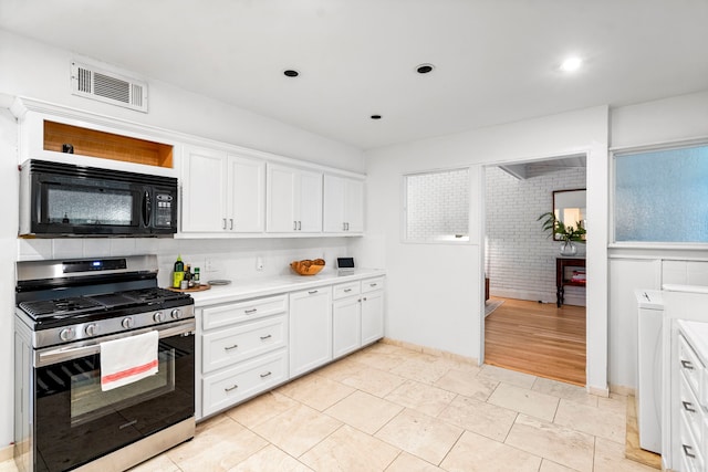 kitchen featuring stainless steel gas range oven, white cabinets, light hardwood / wood-style flooring, and washing machine and dryer