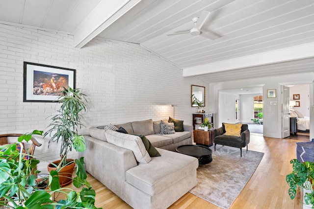 living room featuring light hardwood / wood-style floors, vaulted ceiling with beams, brick wall, and ceiling fan